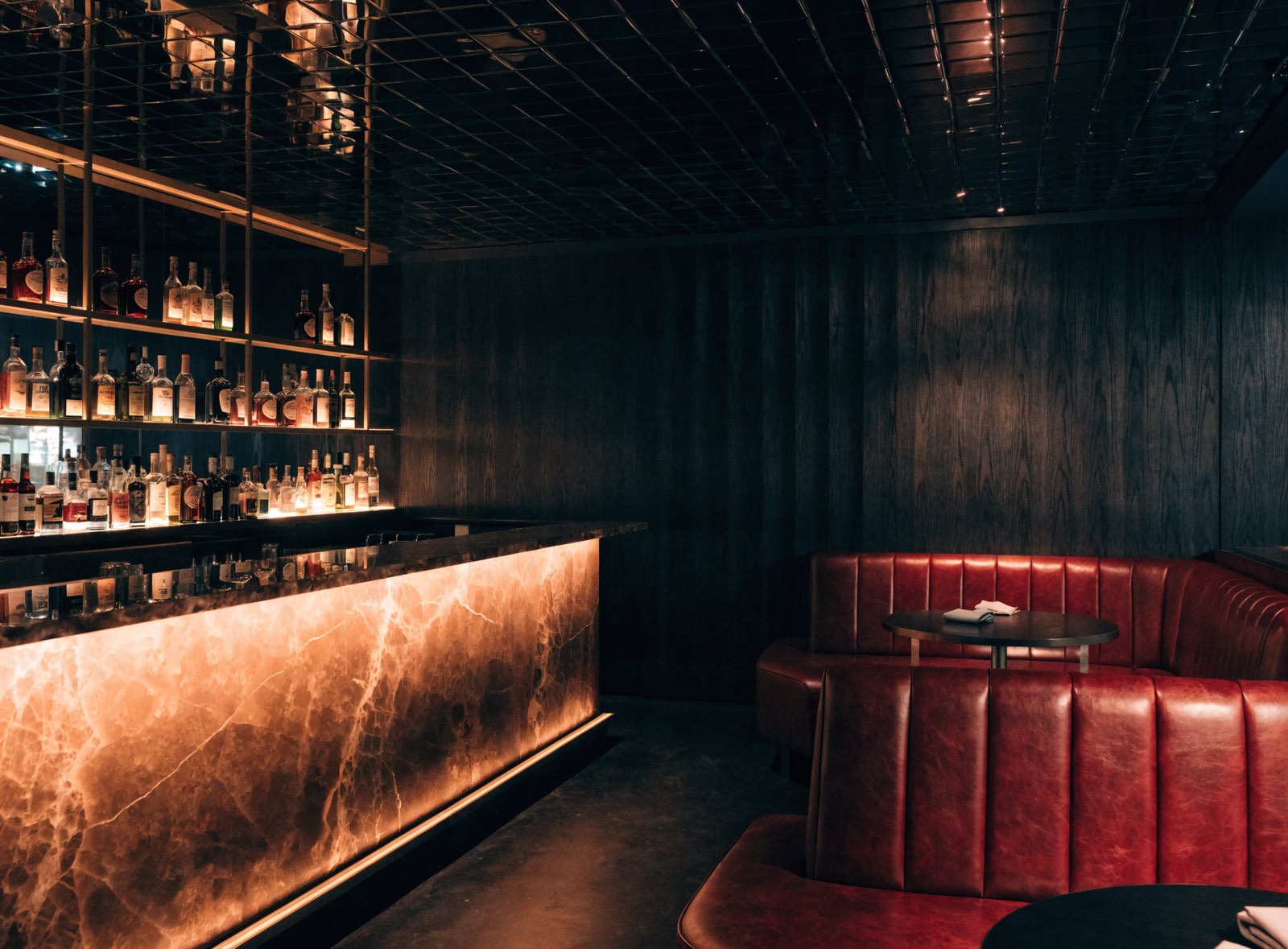 Bar-Interior bei Nacht mit hinterleuchteter Onyx-Theke, dunklem Holz und Messingregalen