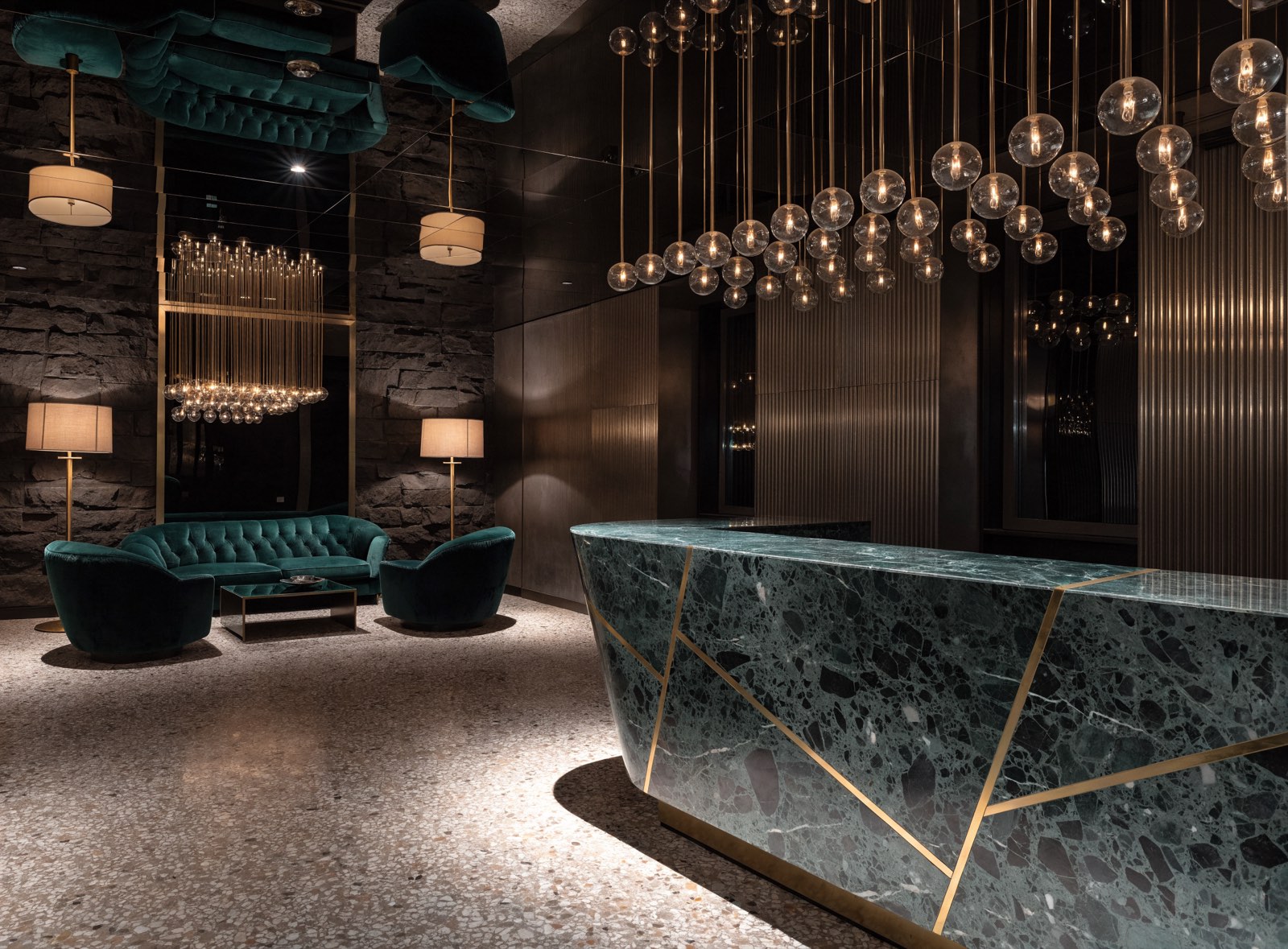 Lobby eines Boutique-Hotels mit grüner Marmortheke, Messingdetails und skulpturalem Leuchter